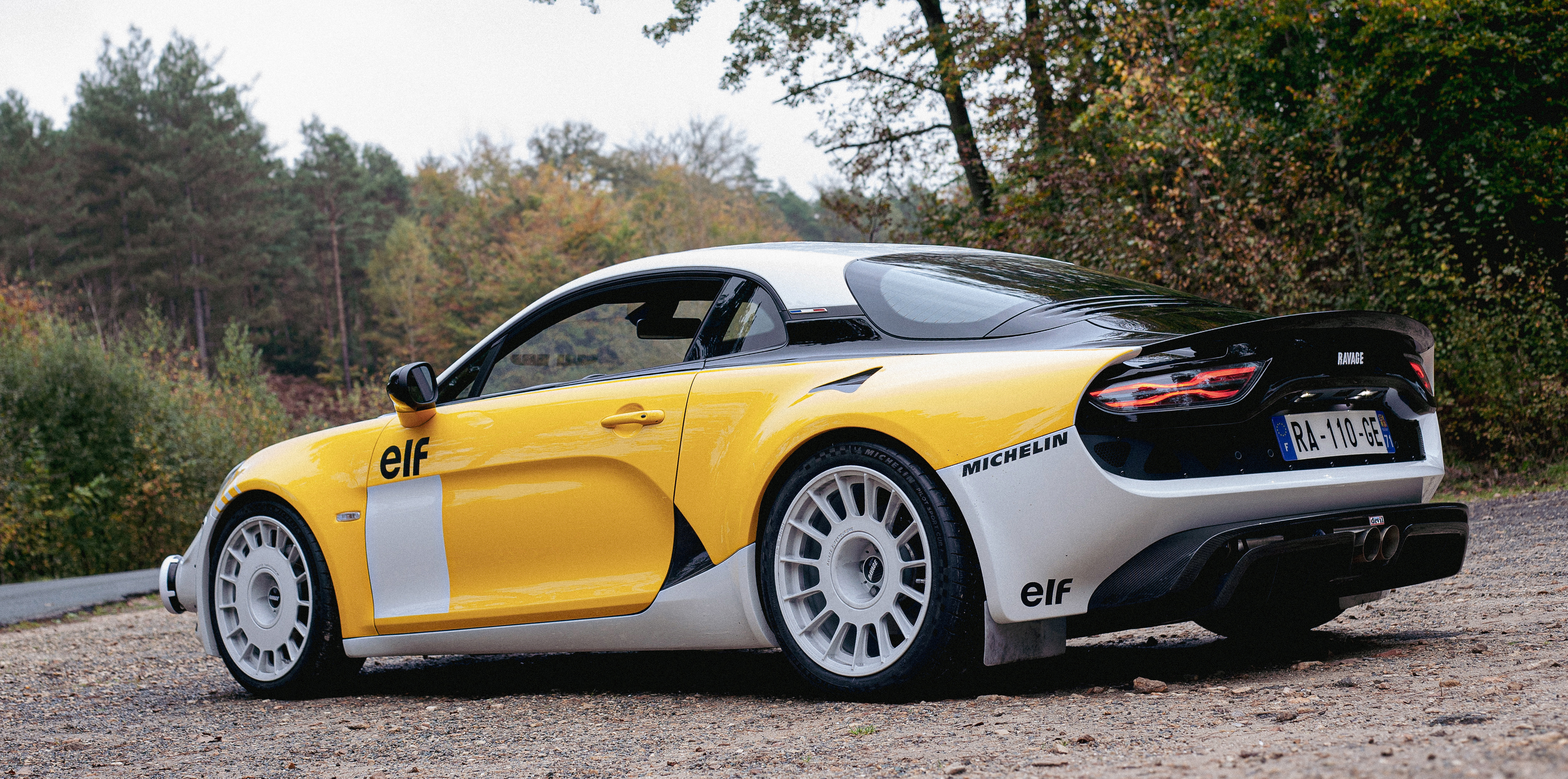 Ravage Groupe 4 jaune et blanc en livrée elf, de trois quarts arrière sur un bas-côté de gravier, jantes rallye blanches et aileron carbone.